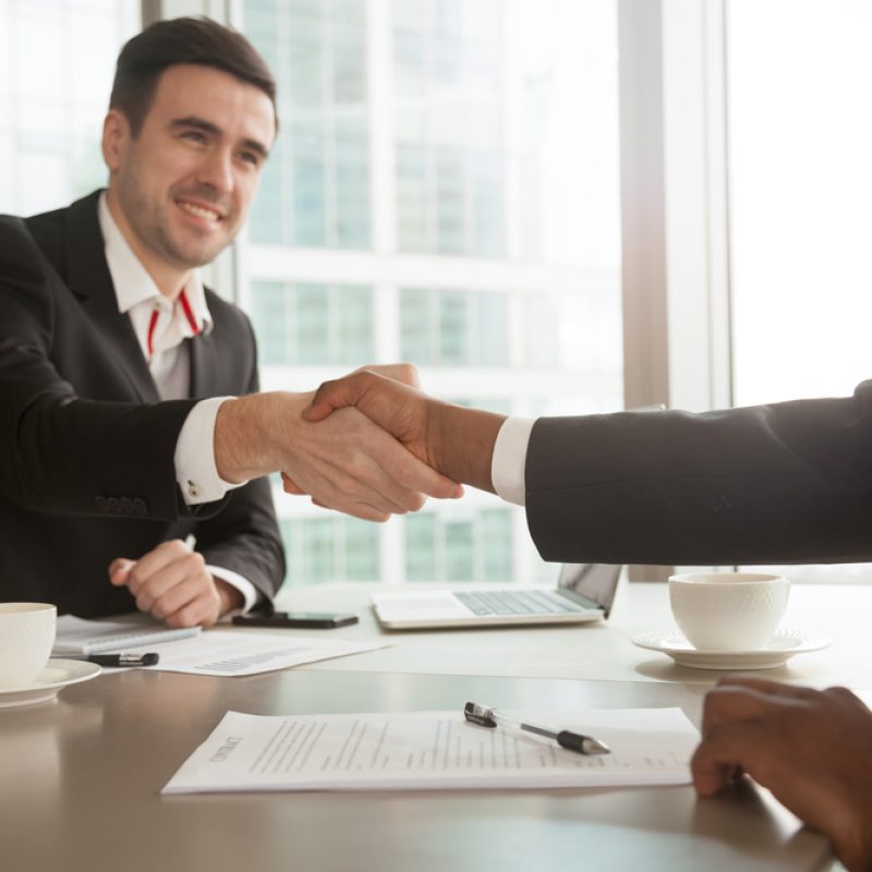 Partners shaking hands after singing contract Close up image of multinational business partners shaking their hands after singing contract at desk in office. Successful business negotiations, accepting good offer, full trust between businessmen